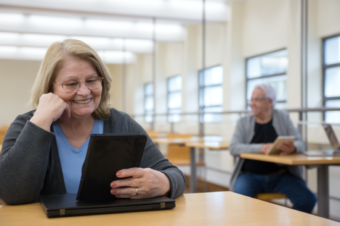 un aula con dos personas mayores usando dispositivos digitales