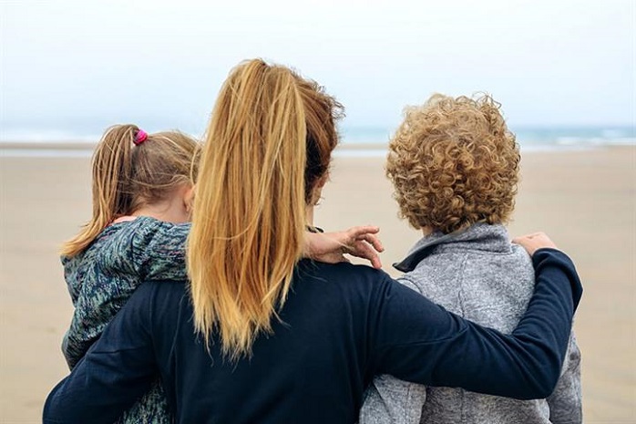 Una mujer de espaldas rodea con sus brazos a una niña y un niño