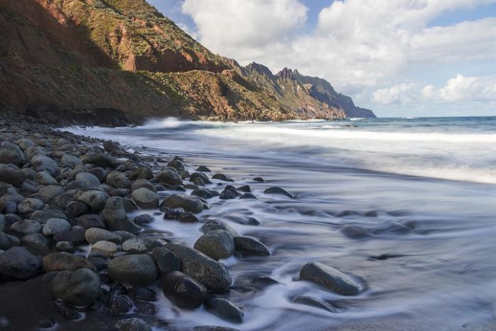 Una playa pedregosa con una montaña al fondo